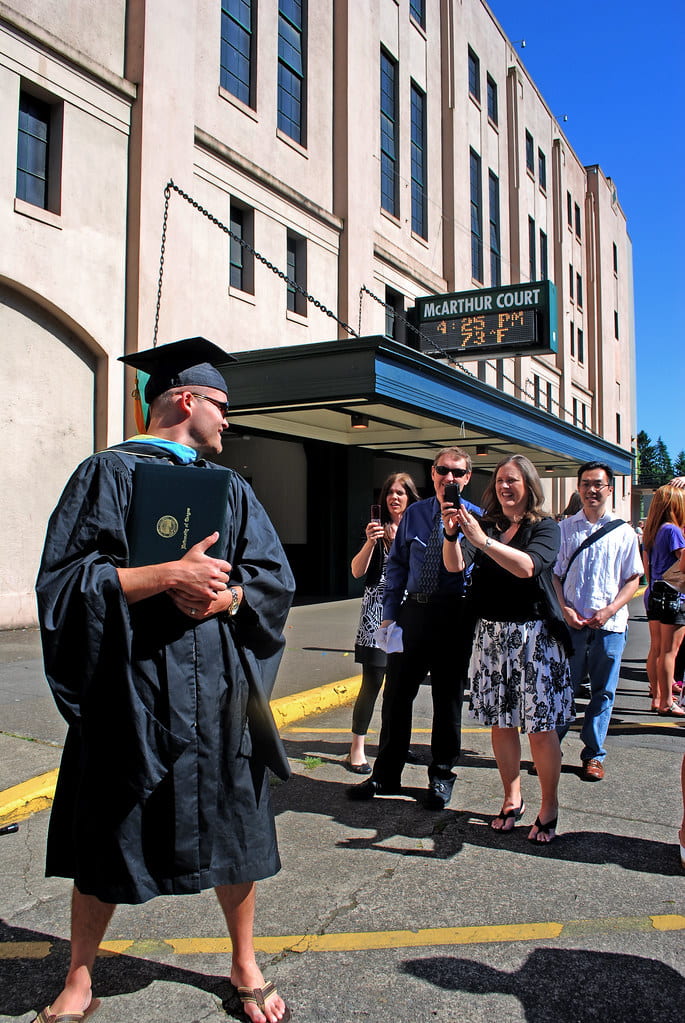 Person in graduation robes getting picture taken in front of building